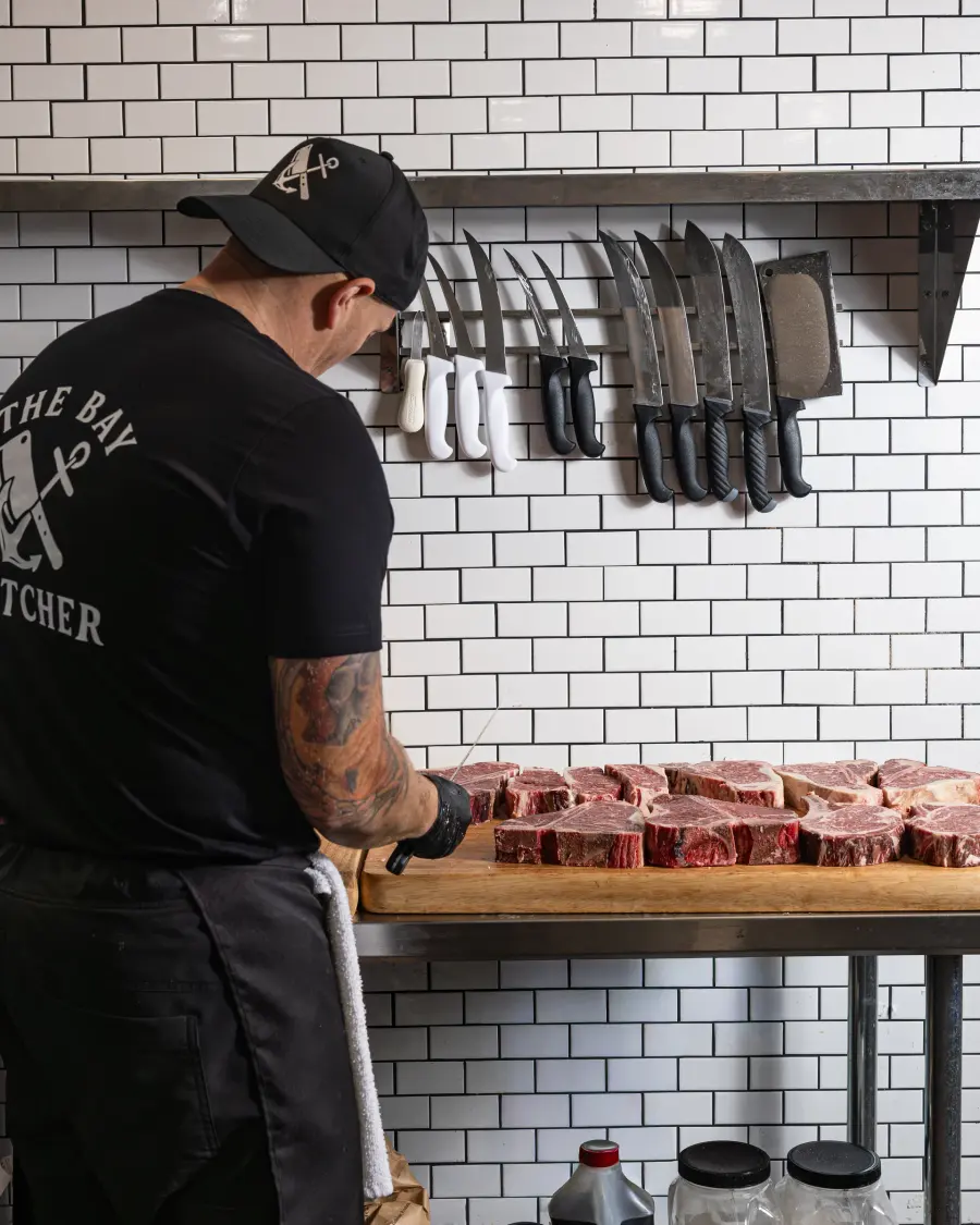 A butcher working the counter beneath a wall of knives